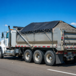 Heavy duty dump truck with a custom tarp securely covering a gravel load on an Alberta highway